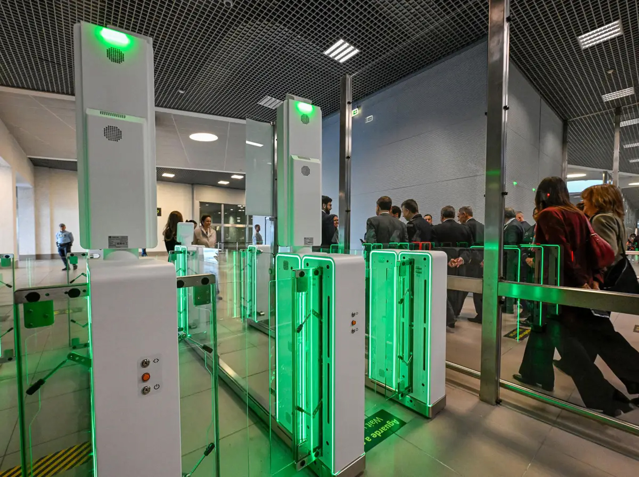 Portões automáticos de controlo de fronteira com luzes verdes e passageiros em fila no aeroporto de Lisboa.