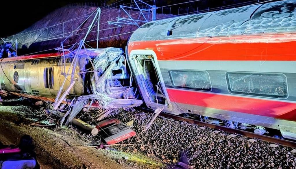Destroços de dois comboios descarrilados à noite, com danos visíveis nas carruagens e destroços espalhados junto à linha férrea, ilustrando a gravidade do acidente ferroviário em Córdova.