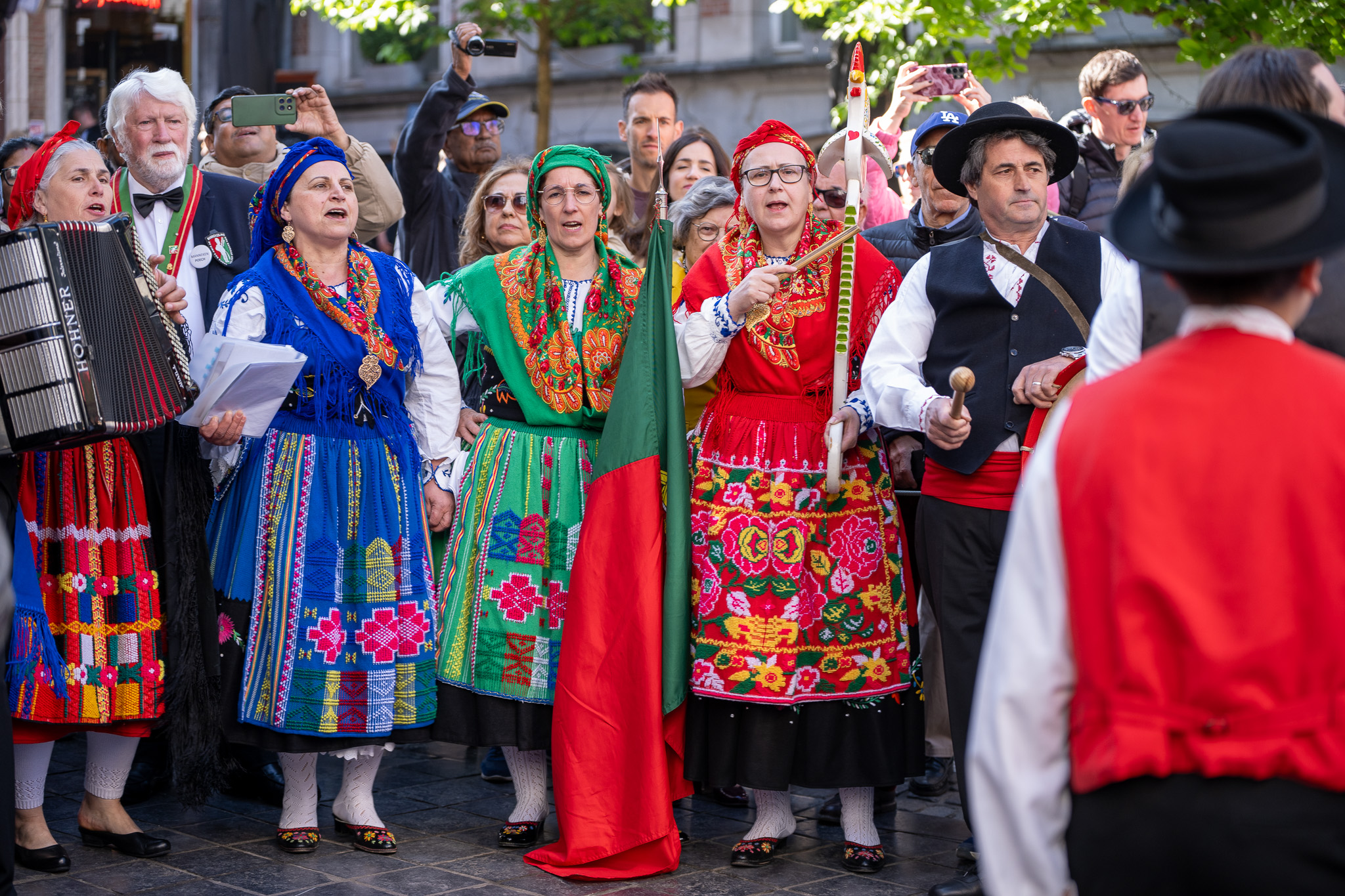 Grupo de pessoas com trajes tradicionais portugueses a cantar e tocar instrumentos numa rua, celebrando a cultura portuguesa num ambiente festivo.