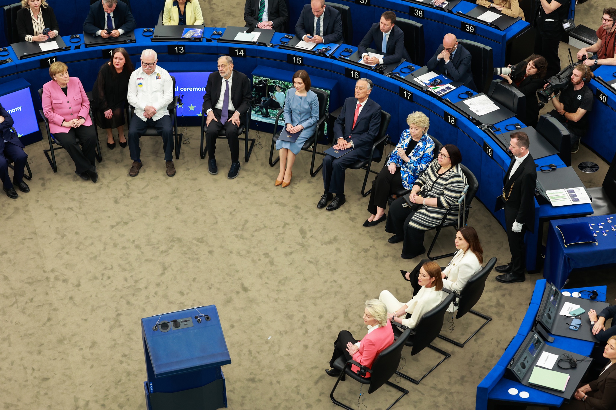 Cerimónia formal no hemiciclo do Parlamento Europeu, com várias pessoas sentadas em semicírculo, durante a entrega de distinções a personalidades europeias.