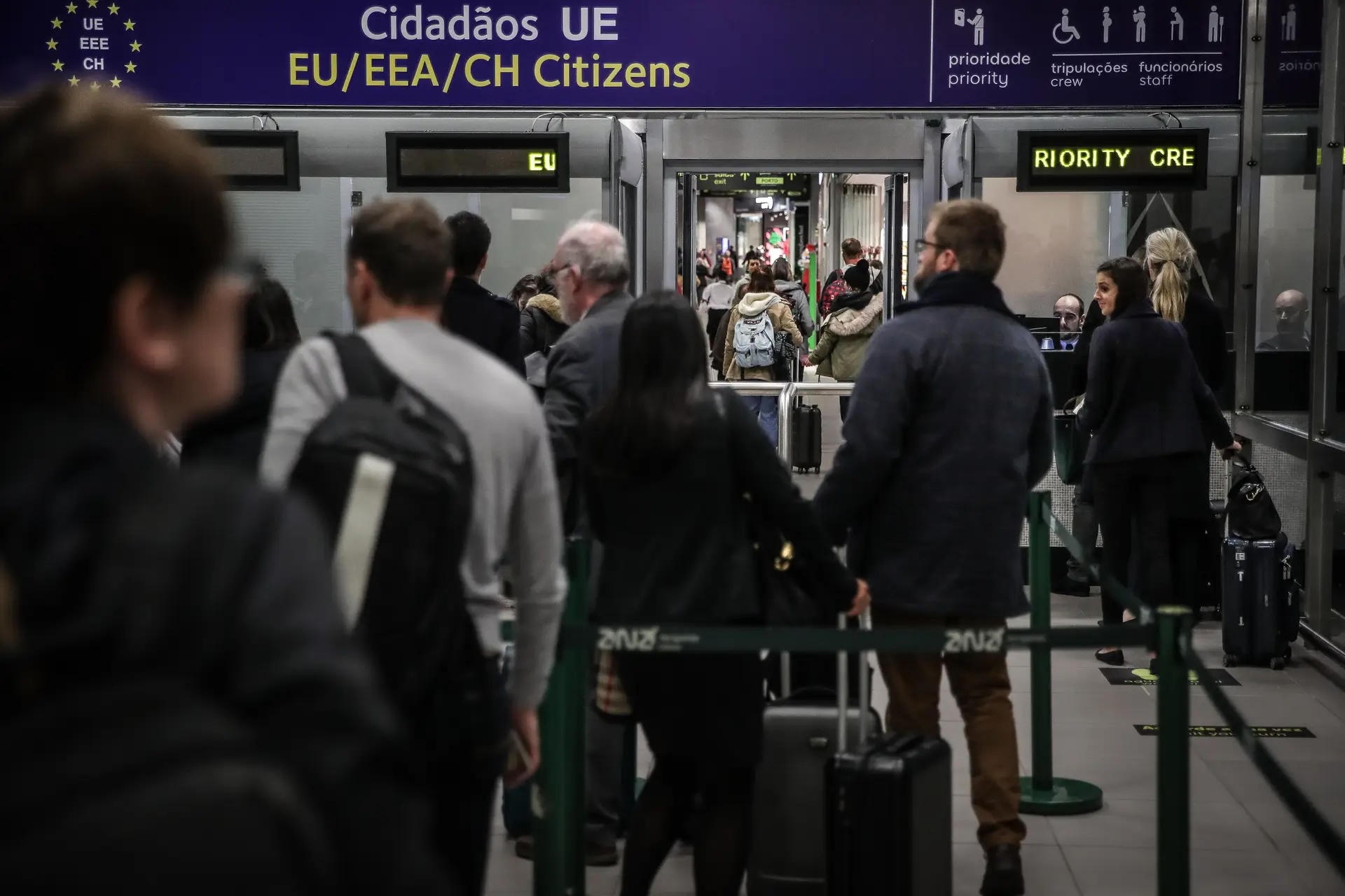 Passageiros em fila numa zona de controlo de fronteiras de aeroporto, junto a uma placa para cidadãos da UE/EEE/Suíça, ilustrando tempos de espera e controlo reforçado referidos no artigo.
