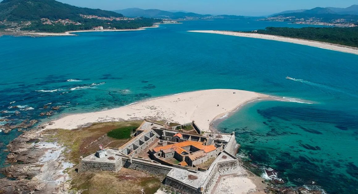 Vista aérea do Forte da Ínsua, uma fortificação de pedra situada numa pequena ilha rochosa junto à foz do rio Minho, rodeada por areia e mar.